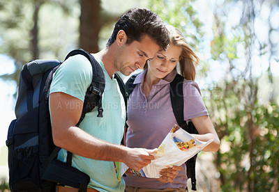 Buy stock photo A young couple studying their map while hiking through the woods