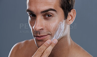 Buy stock photo Studio shot of a handsome young man applying cream to his face