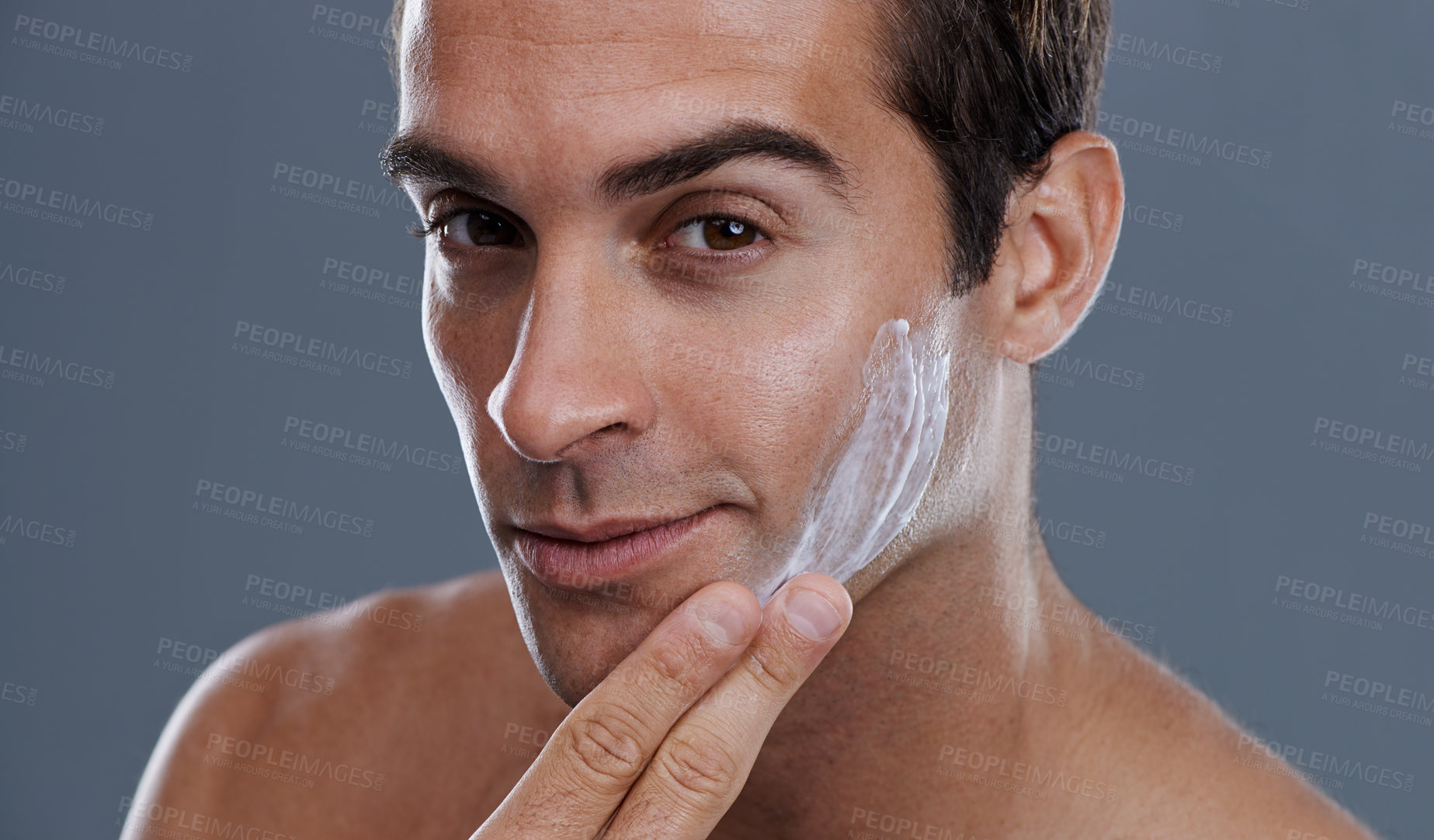 Buy stock photo Studio shot of a handsome young man applying cream to his face