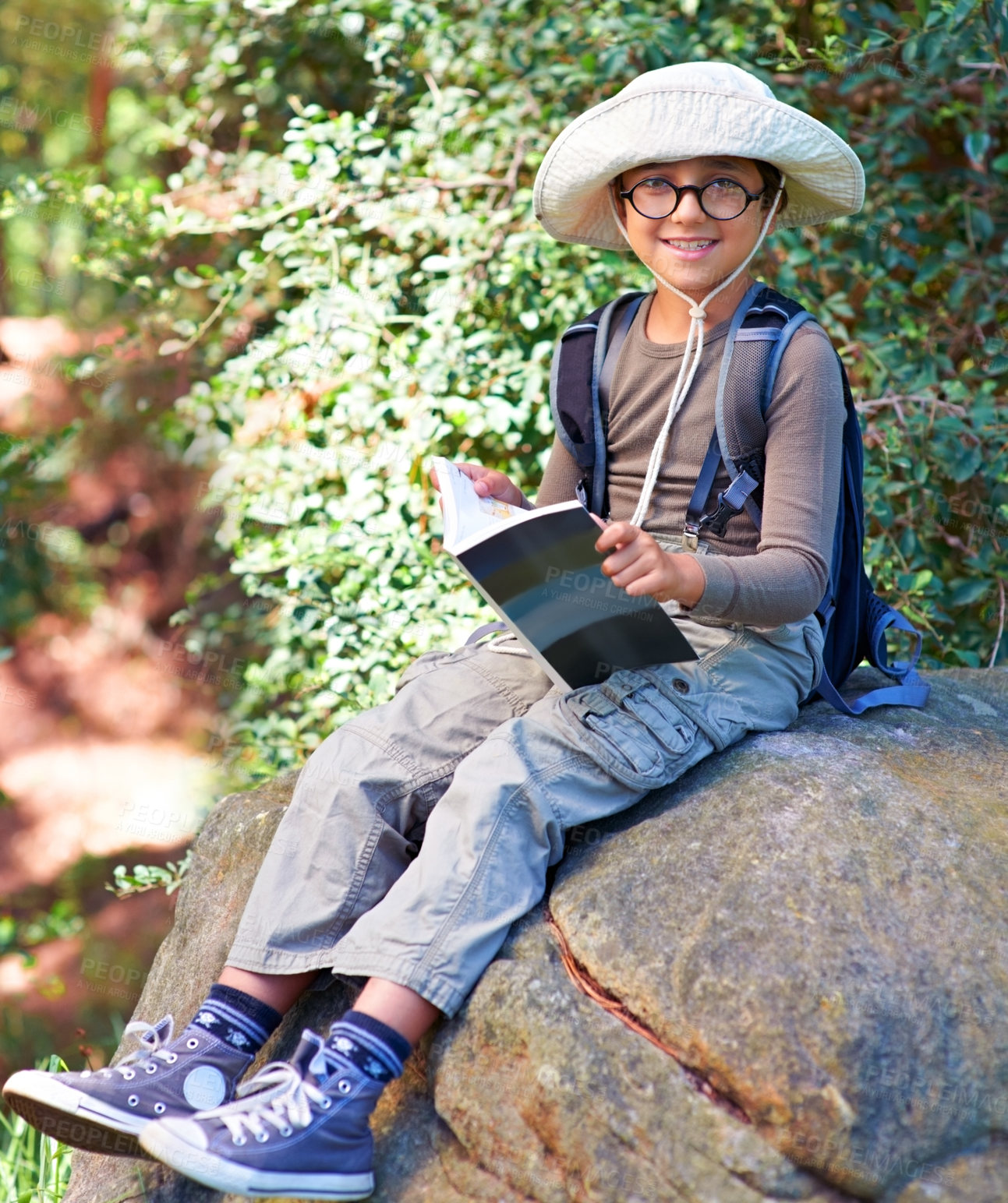 Buy stock photo Boy, kid and hiking, relax on rock and book for reading, backpacking and adventure outdoor. Student on school field trip, nature and forest for discovery and exploration, smile in portrait and travel