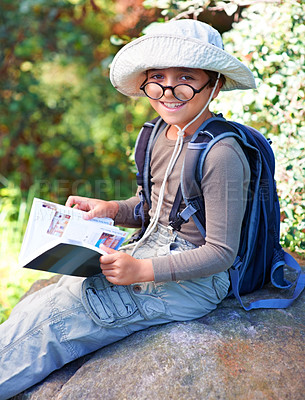 Buy stock photo Boy, kid and hiking, book for reading and relax on rock, backpacking and adventure outdoor. Student on school field trip, nature and forest for discovery and exploration, smile in portrait and travel