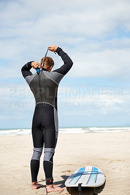 Buy stock photo Surfer, man and getting ready with surfboard on beach with wetsuit, blue sky and dressing with mock up space. Rear view, athlete and person by ocean for training, surfing workout and extreme sports 