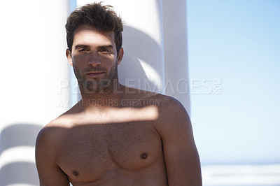 Buy stock photo Handsome, shirtless and portrait of man outdoor by pillars at beach with confidence on vacation. Serious, model and attractive young male person by wall at ocean or sea for holiday or weekend trip.