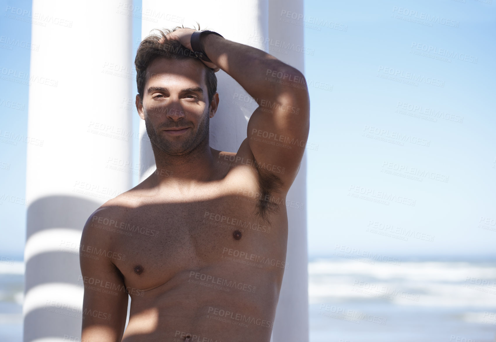Buy stock photo Smile, shirtless and portrait of man outdoor by pillars at beach with confidence on vacation. Happy, model and handsome young male person by wall at ocean or sea for holiday or weekend trip.