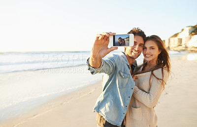Buy stock photo Shot of an affectionate young couple taking a selfie at the beach