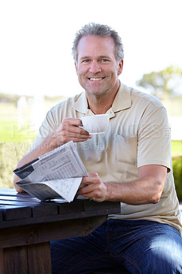 Buy stock photo Portrait of a mature man enjoying a cup of coffee outside while reading a newspaper