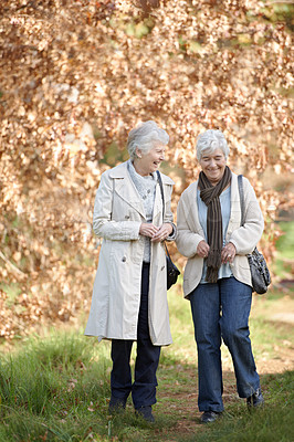 Buy stock photo Senior women, walk or conversation in nature by autumn leaves, together or laughing on retirement in park. Elderly friends, happy or communication on vacation in england, care or exercise in outdoor