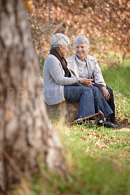 Buy stock photo Senior women, listening or talking in nature by autumn leaves, happy or bonding on retirement in outdoor. Elderly friends, smile or discussion on vacation in forest, care or social in woods on rock