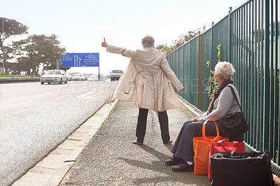 Buy stock photo Senior people, hitchhiking and traveling on road, retirement and waiting for taxi or cab in city. Elderly women, back and outdoor journey or trip in town, friends and roadside assistance on street