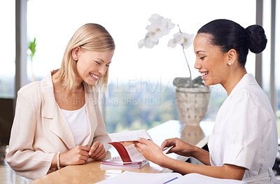 Buy stock photo A young woman looking at a brochure showed to her by a spa employee