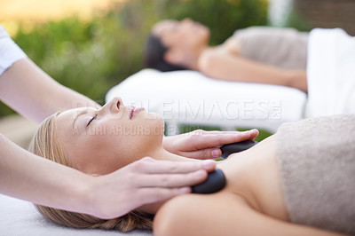 Buy stock photo Young woman, hands and hot stone massage in spa, outdoor and wellness on bed for physical therapy. People, heat or masseuse for body treatment for detox, pain or muscle comfort with health at resort