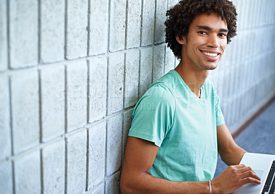Buy stock photo A young man using his laptop and smiling at the camera