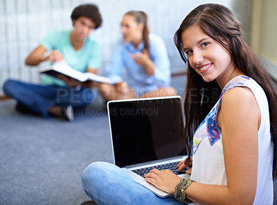 Buy stock photo A young student working on her laptop while her friends sit with a textbook in the background