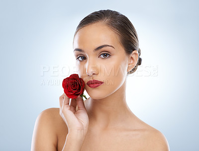 Buy stock photo Woman, portrait and red rose in natural skincare, beauty or cosmetics on a blue studio background. Face of young female person or model with flower, lipstick or makeup glow for facial care on mockup