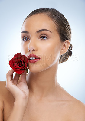 Buy stock photo Woman, face and red rose with makeup in skincare, beauty or cosmetics on a blue studio background. Young female person or model with flower, petals and lipstick for glow, care or facial treatment