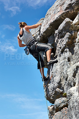 Buy stock photo A young woman climbing up a rock face while framed against a blue sky