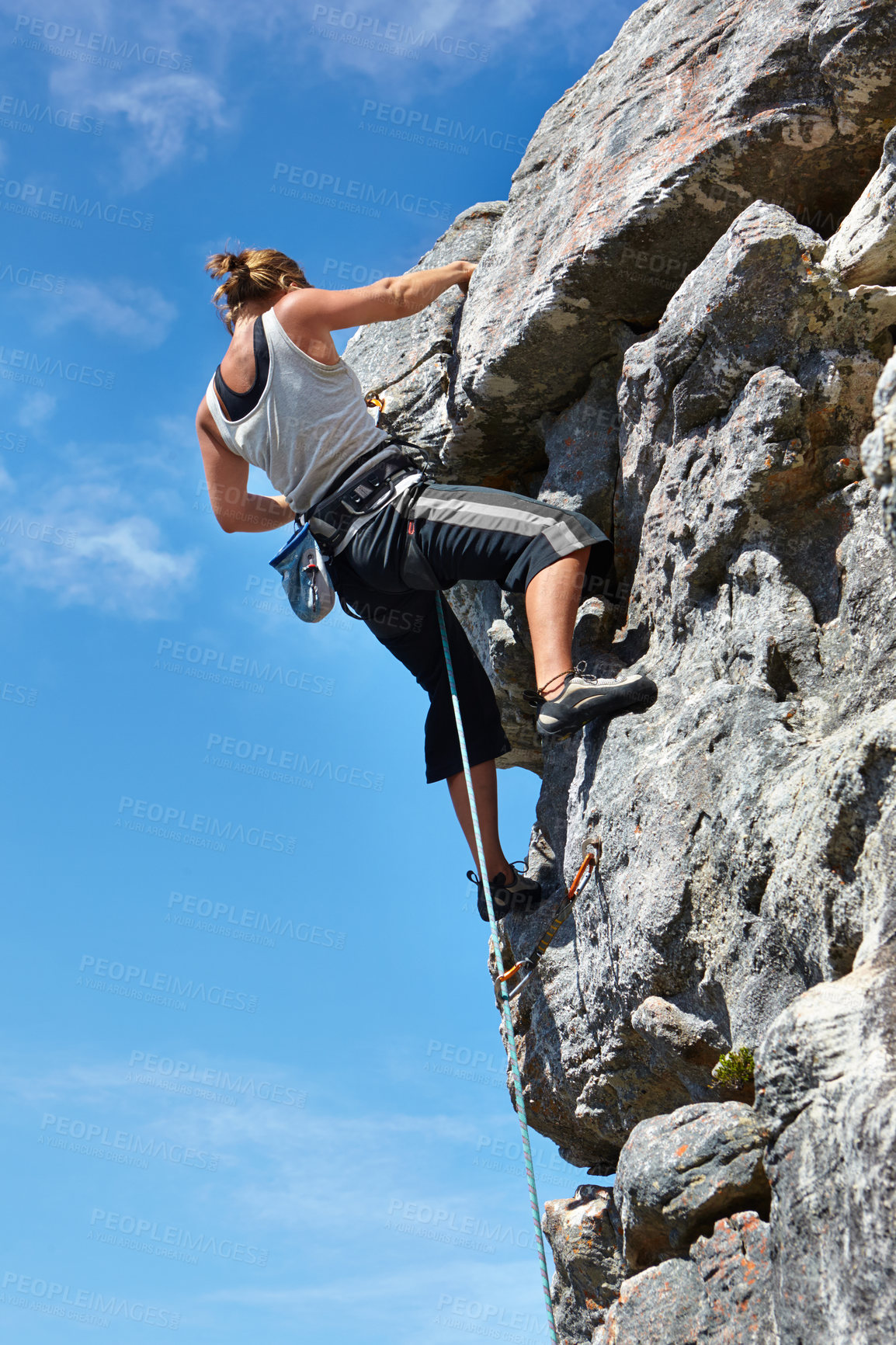 Buy stock photo A young woman climbing up a rock face while framed against a blue sky