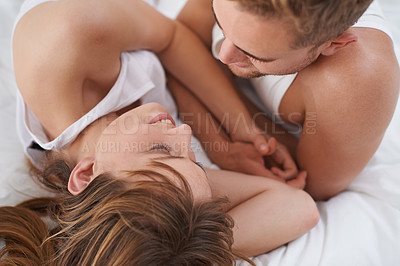 Buy stock photo A young couple in love lying in bed and looking lovingly at each other