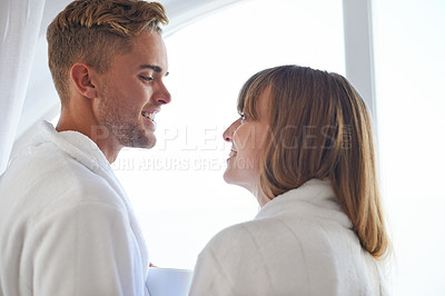 Buy stock photo Couple, morning and happy in robe together with love, smile and eye contact in home or honeymoon. Man, woman and partnership with trust by window in house, connect and romance relationship with care