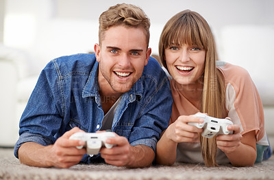 Buy stock photo A young couple playing games together while lying in their living room