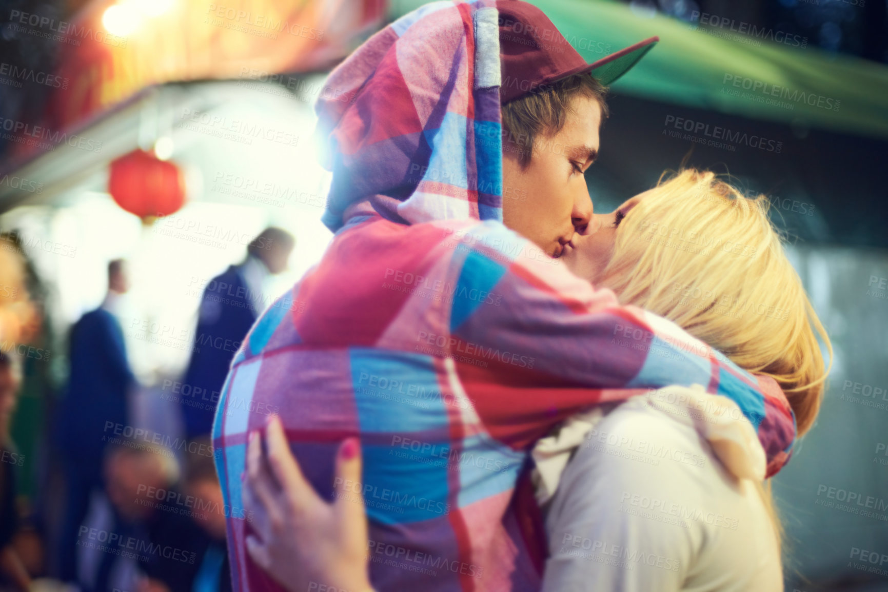 Buy stock photo Couple, hug and kiss with love at music festival for bonding, affection or celebration together. Happy, woman and man with cap at colourful event for enjoyment, adventure or experience together