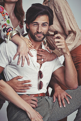 Buy stock photo Studio shot of an attractive man in retro 70s wear surrounded and being touched by women while smoking his pipe