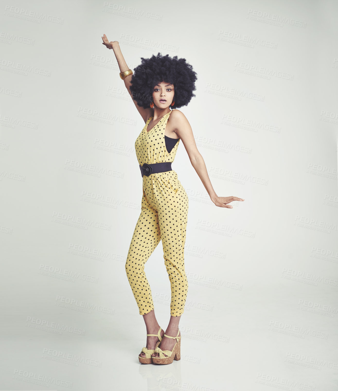 Buy stock photo A young woman wearing a 70s retro jumpsuit and striking a disco pose while in the studio