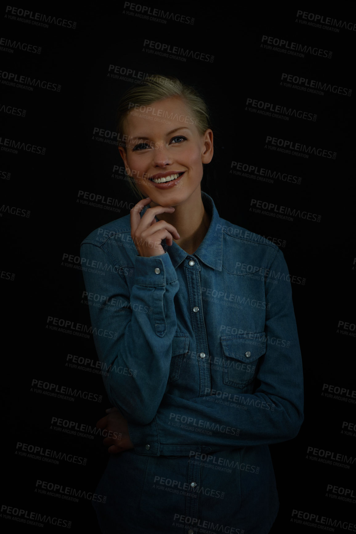 Buy stock photo Portrait, young woman standing with her hand on her chin and wearing a denim shirt in studio. Female person against black background, smiling and positive thoughts to brighten up a dark world 