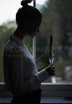 Buy stock photo Woman, feather and window for writer in home, dark room and creative for abstract or artistic pose. Female artist, writing and shadow with thinking, fashion and mysterious editor for literature