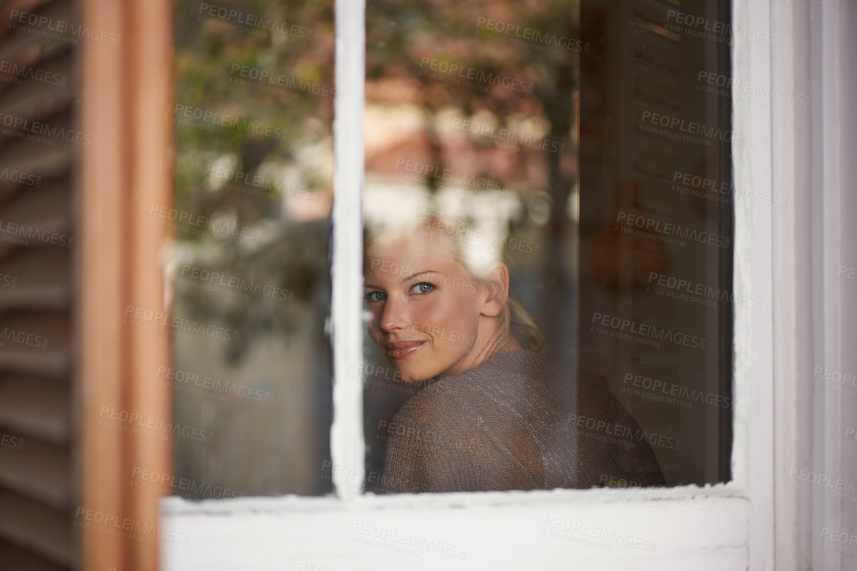 Buy stock photo A young woman looking through her window