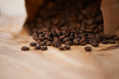 Buy stock photo Table, closeup and fresh roasted coffee beans, spilling from a paper bag onto a vintage wood counter with copy space. Studio, aromatic bitter caffeine to feel refreshed with hot, refreshing beverage
