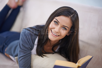 Buy stock photo Portrait of an attractive young woman lying on a sofa and reading a novel