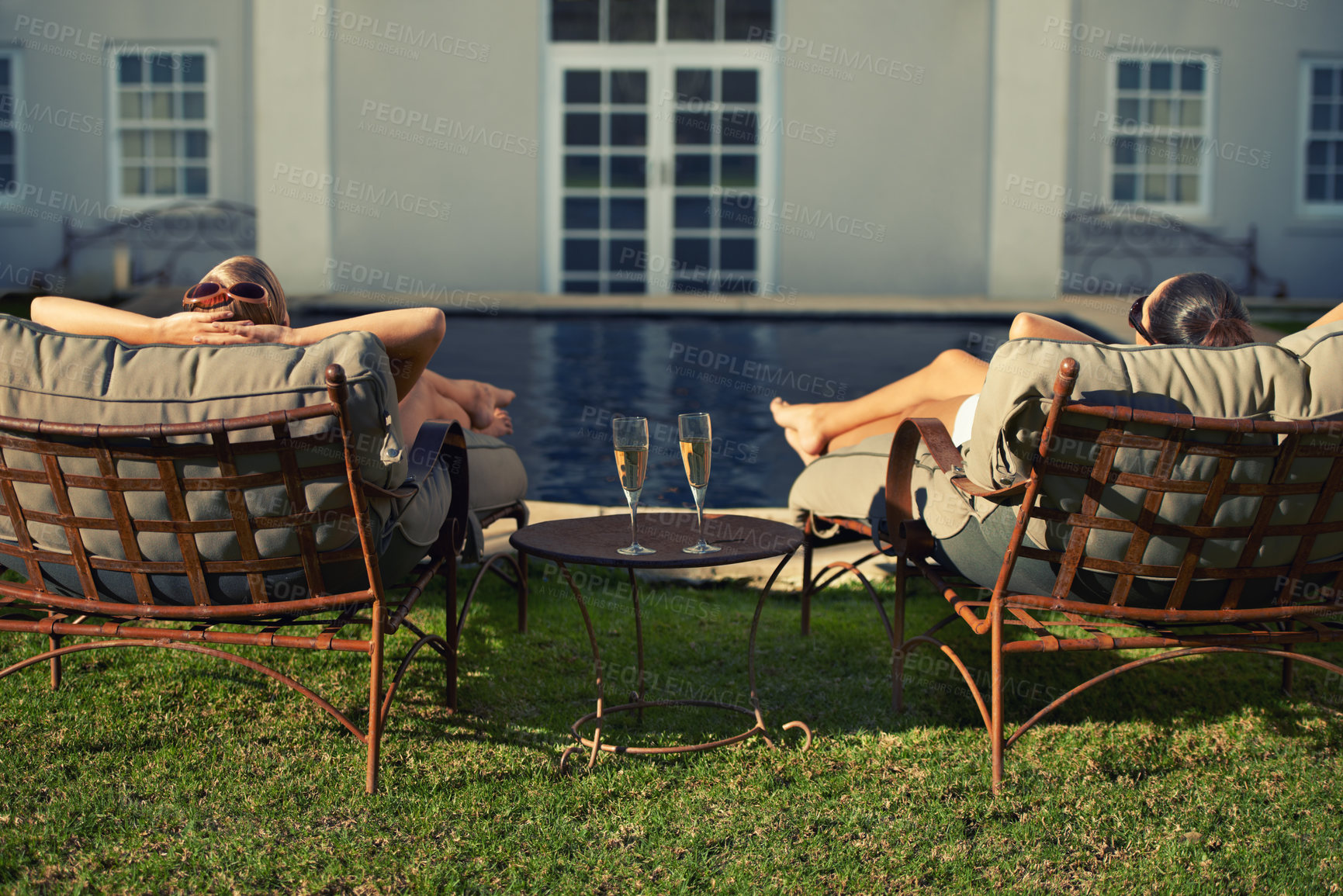 Buy stock photo Rear view of two young woman relaxing on loungers facing the pool