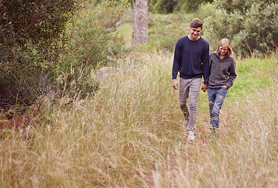 Buy stock photo A young couple strolling hand in hand through a meadow