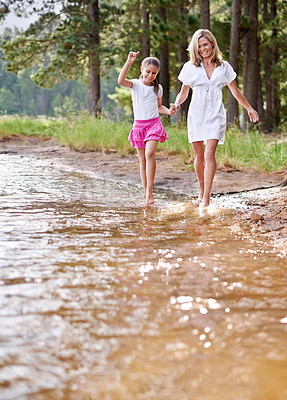 Buy stock photo Mother, daughter and happiness outdoor in river for bonding, support or holding hands on holiday in nature. Family, woman and girl child with smile or adventure on vacation, travel and lake with love