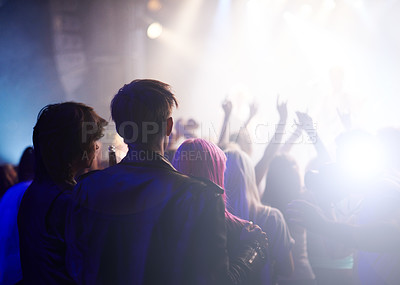 Buy stock photo Dance, rock and friends in crowd at music festival from back, watching live band performance on stage. Audience in arena, lights and group of people at party, fans of musician at concert together.