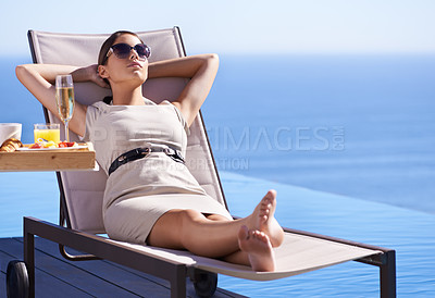 Buy stock photo A posh young woman reclining on a deck chair with her hands behind her head