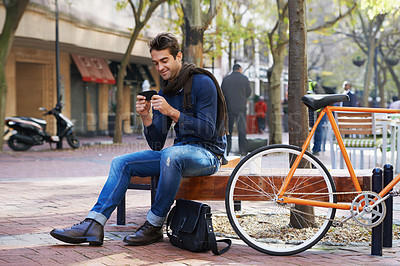 Buy stock photo Phone, bike and business man in city, sitting on bench for break with social media browsing or app. Smile, contact and bicycle with confident young employee typing text message outdoor in urban town