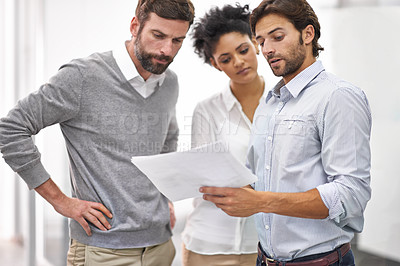 Buy stock photo Shot of three young businesspeople standing in his office and discussing paperwork