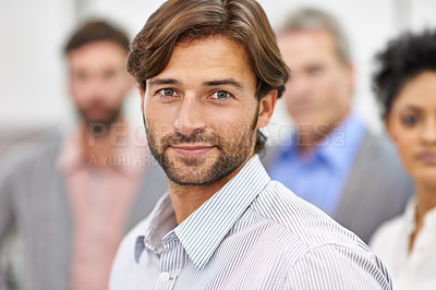 Buy stock photo Cropped shot of a handsome young man standing with his colleagues blurred in the background