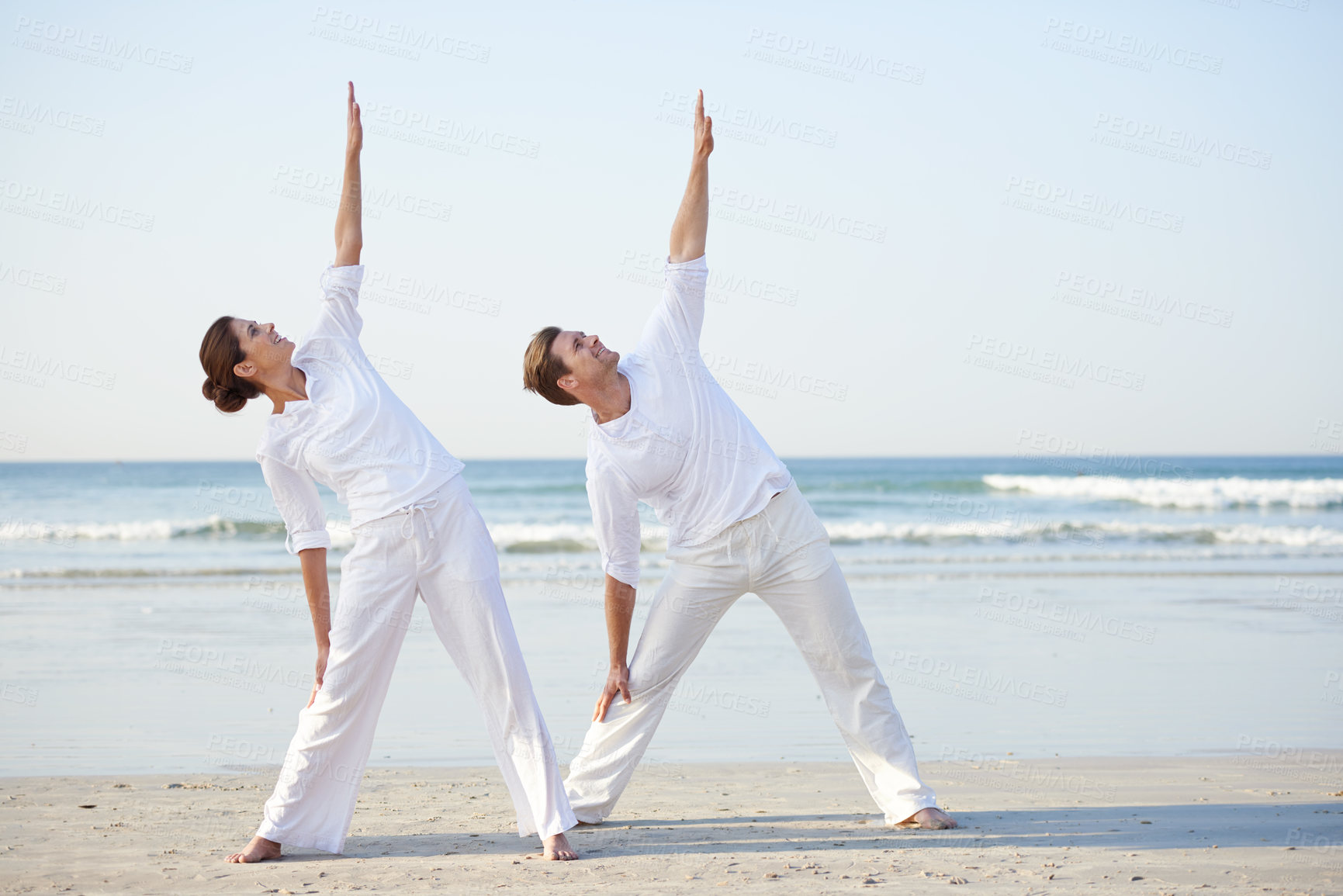 Buy stock photo A young couple practising yoga on the beach