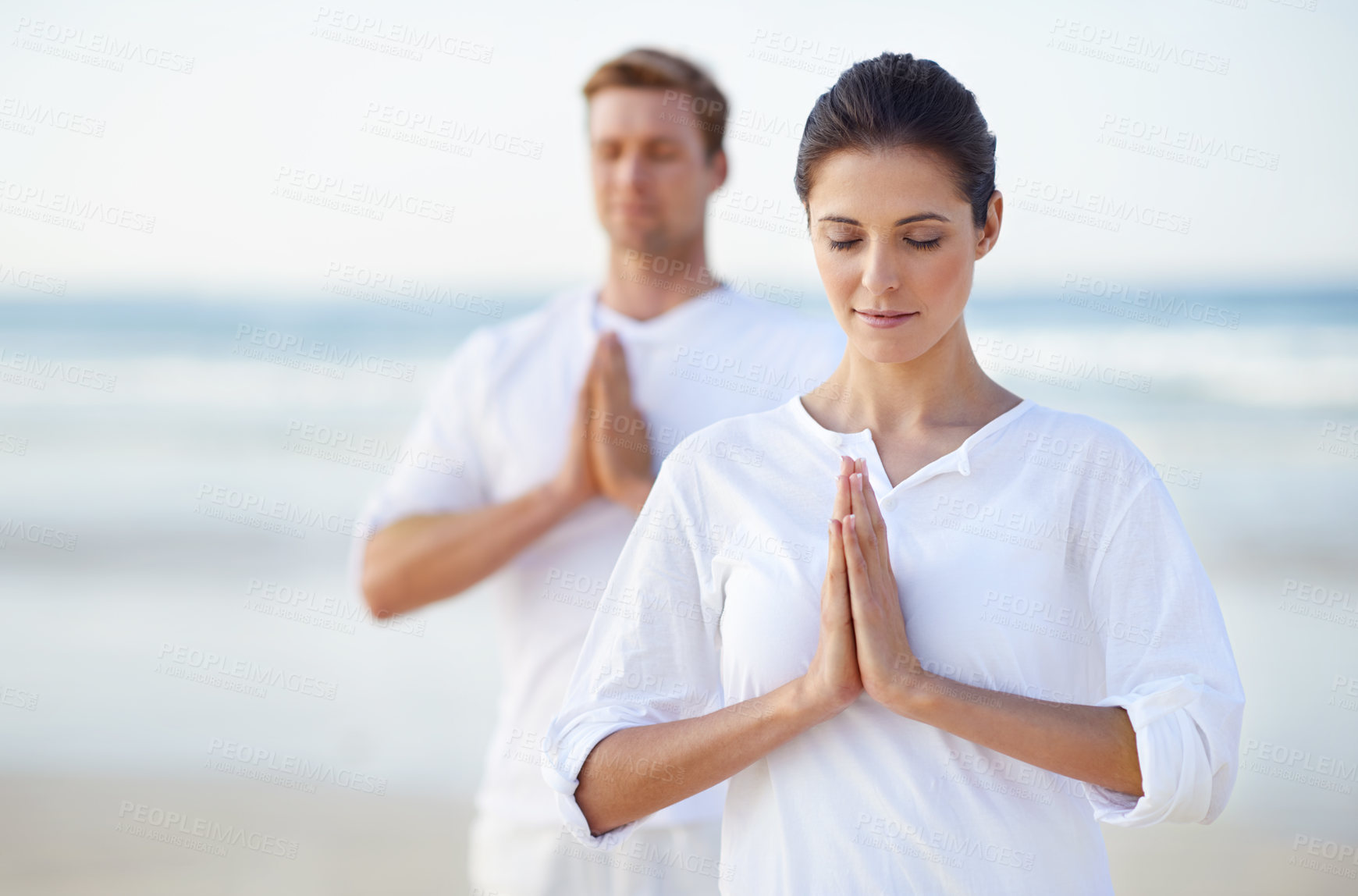 Buy stock photo A young couple practising yoga on the beach