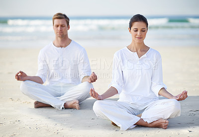 Buy stock photo A young couple practising yoga on the beach