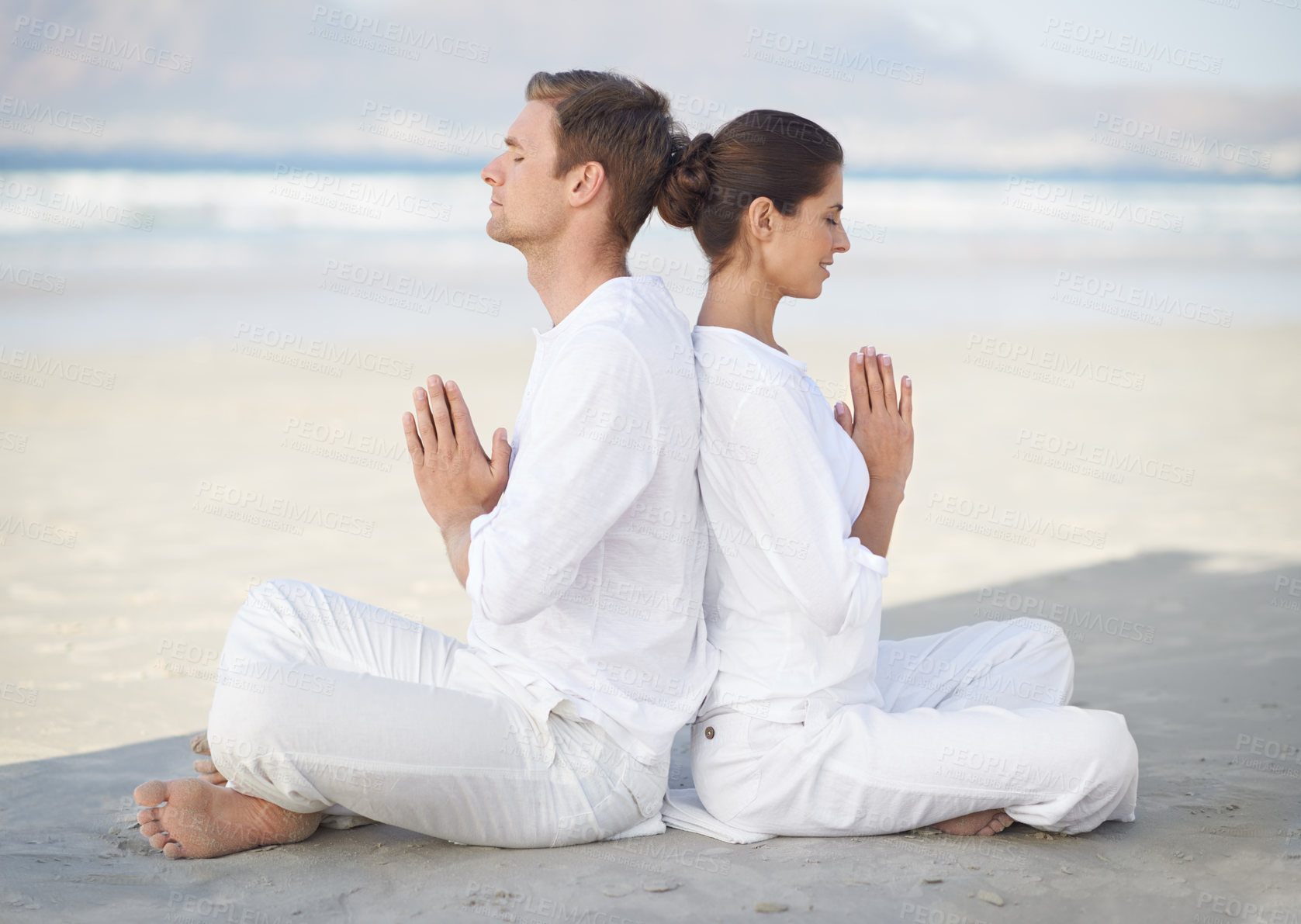 Buy stock photo A young couple practising yoga on the beach