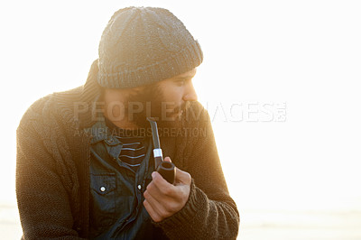 Buy stock photo Holiday, man and smoking a pipe on beach, thinking and sunrise with tobacco habit in winter. English guy, nicotine addiction or vintage smoker for calm, satisfaction or vacation by ocean in cape town