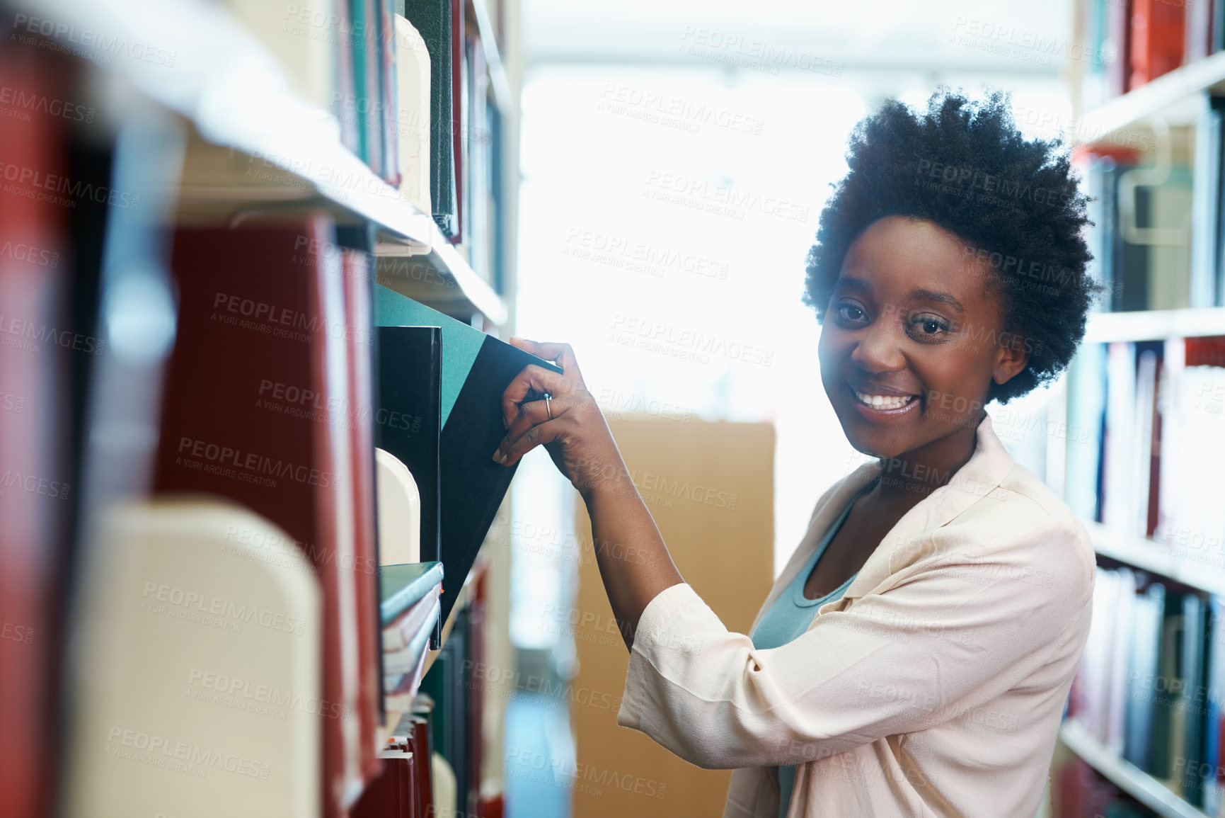 Buy stock photo A young woman selecting some books in the library