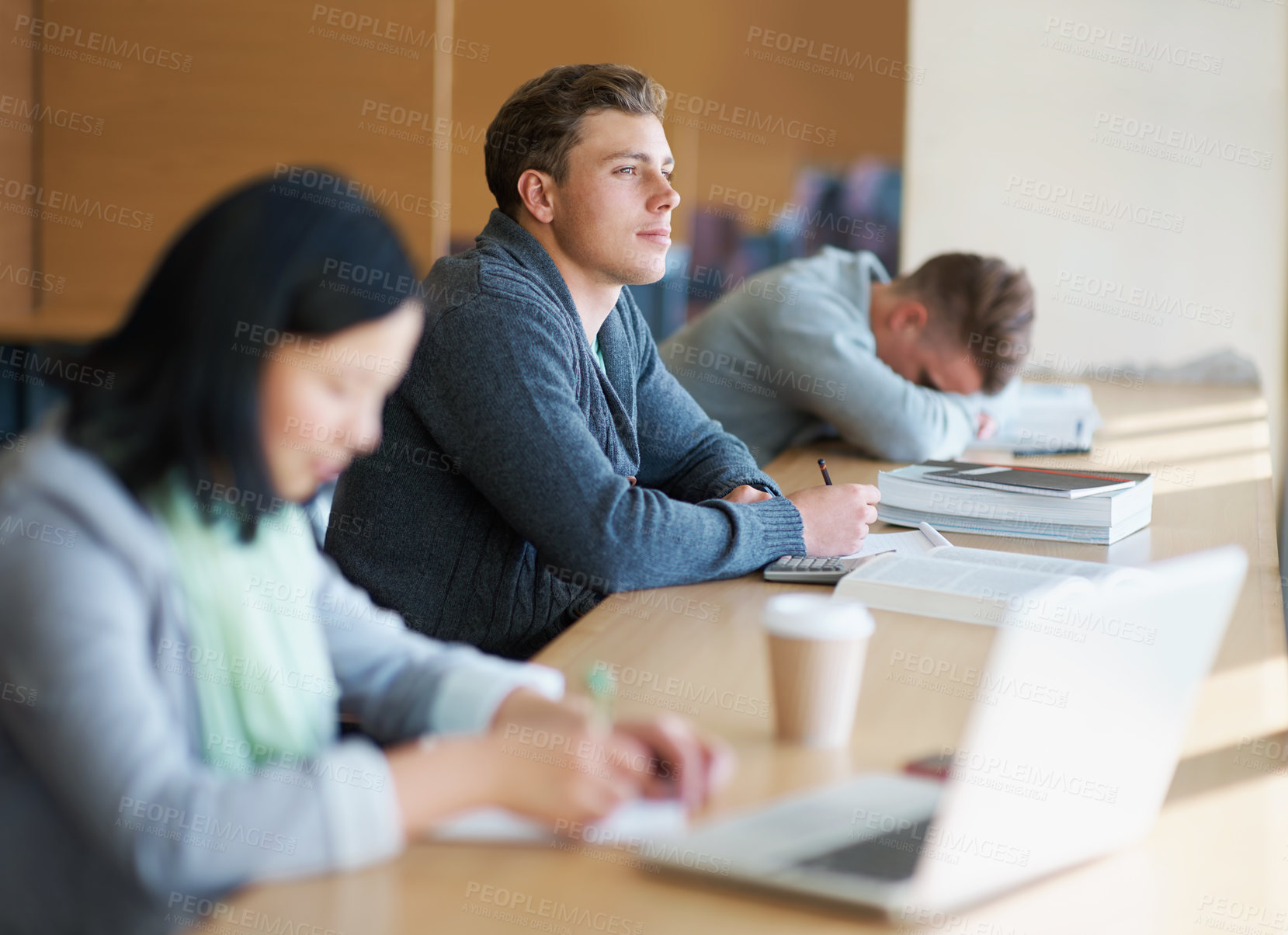 Buy stock photo A young man studying the library with other students