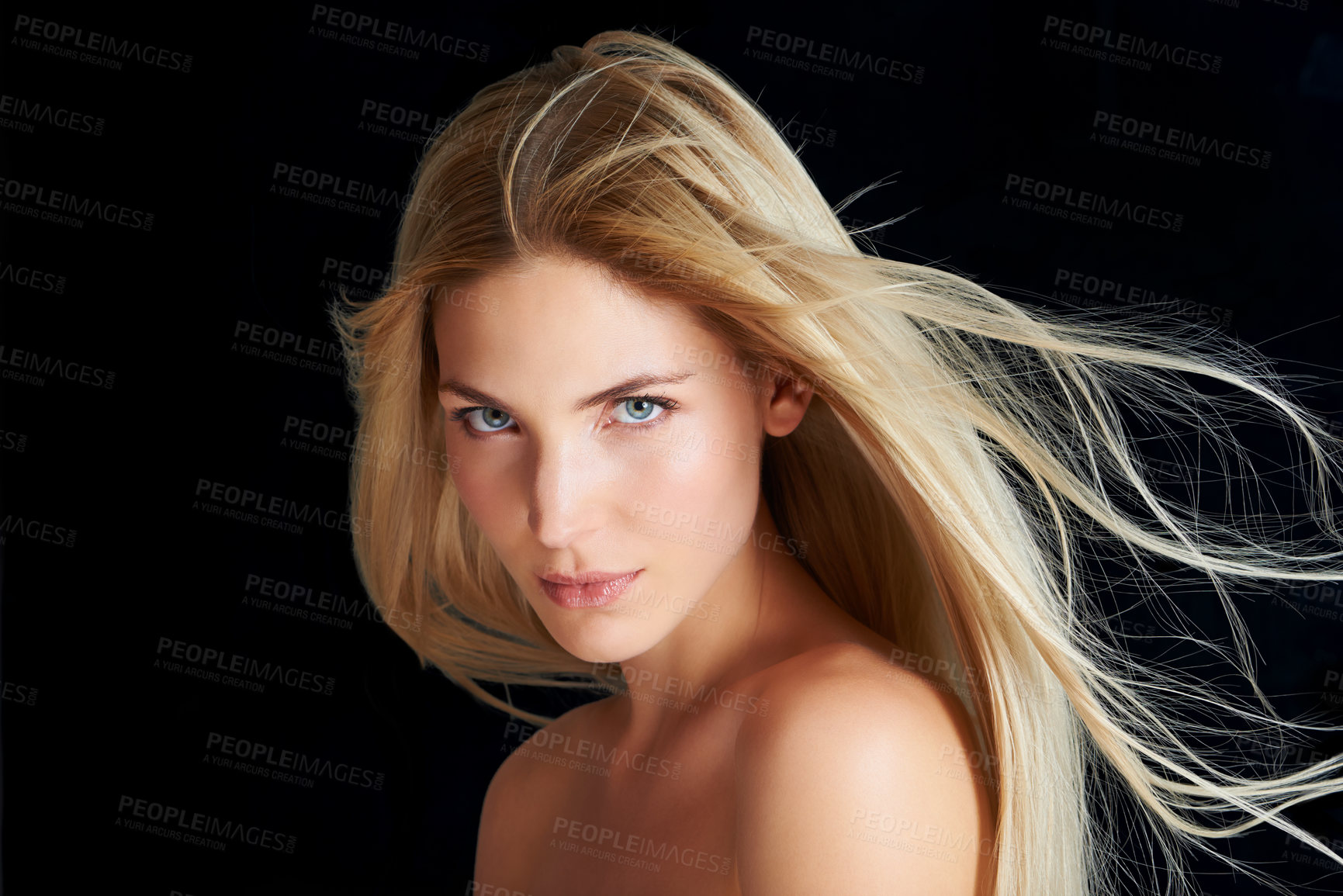Buy stock photo A beautiful young woman posing in front of a black background with the wind blowing through her hair