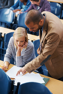 Buy stock photo Shot of a college teacher pointing something out on a students paper