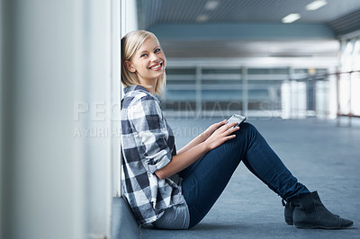 Buy stock photo Shot of a young female student sitting against the wall in a university hall